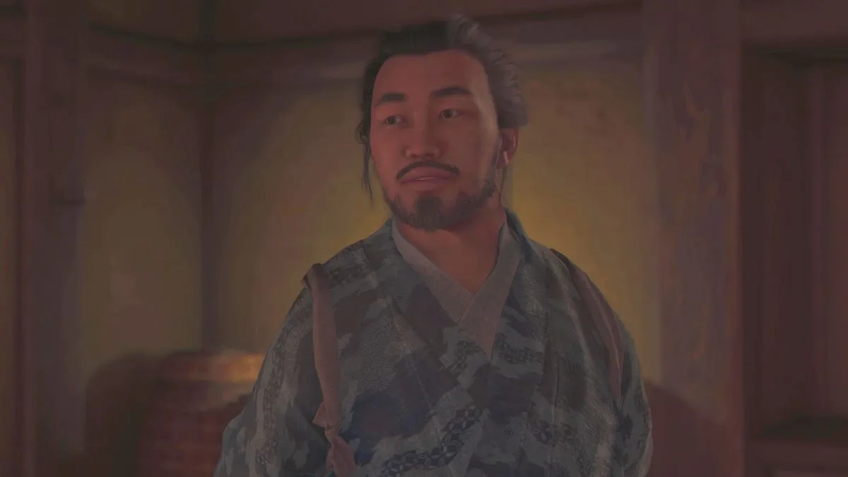 Assassin's Creed Shadows upgrade weapons armour - Heiji the blacksmith about to speak, stood inside a building in the hideout.